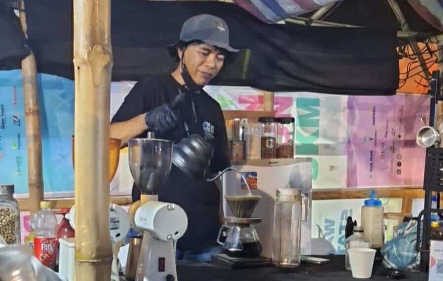 📷 Menjadi seorang barista tidak semudah yang dibayangkan, tetapi juga bukan hal yang mustahil. Dia harus punya pemahaman tentang kopi, keterampilan meracik, dan merawat peralatan. Ori Dar sedang meracik kopi pesanan bule saat Lakey Fest 2025. (Ori Dar).